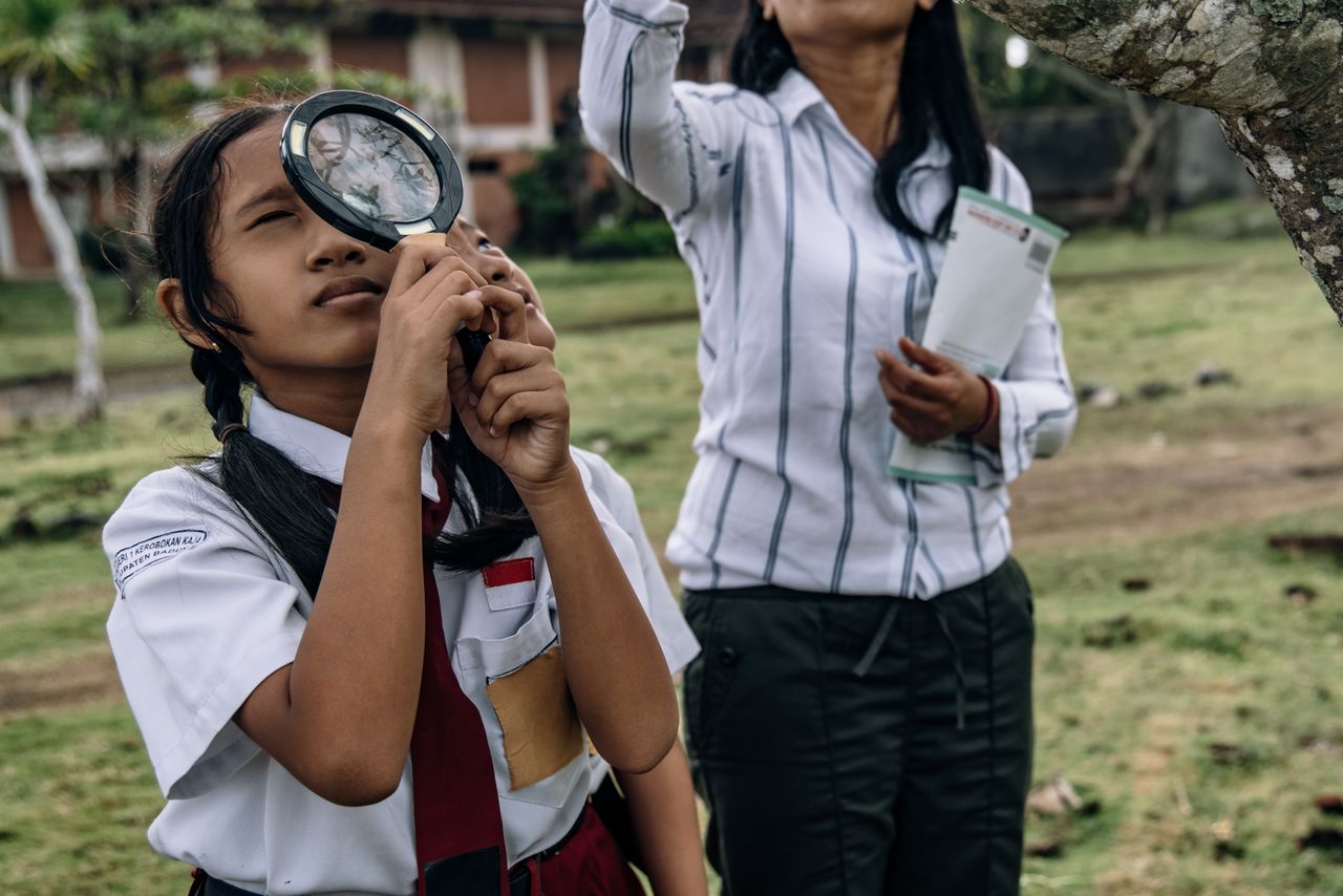 Services Students in school uniforms using a magnifying glass for outdoor exploration. Educational outdoor activity.