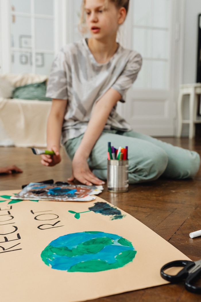 About Teenage girl working on a recycling-themed art project indoors, emphasizing environmental awareness.
