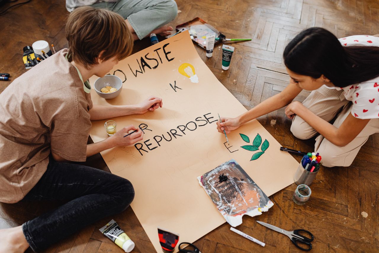 About Two teenagers creatively paint a poster promoting eco-friendly practices like recycling and repurposing.